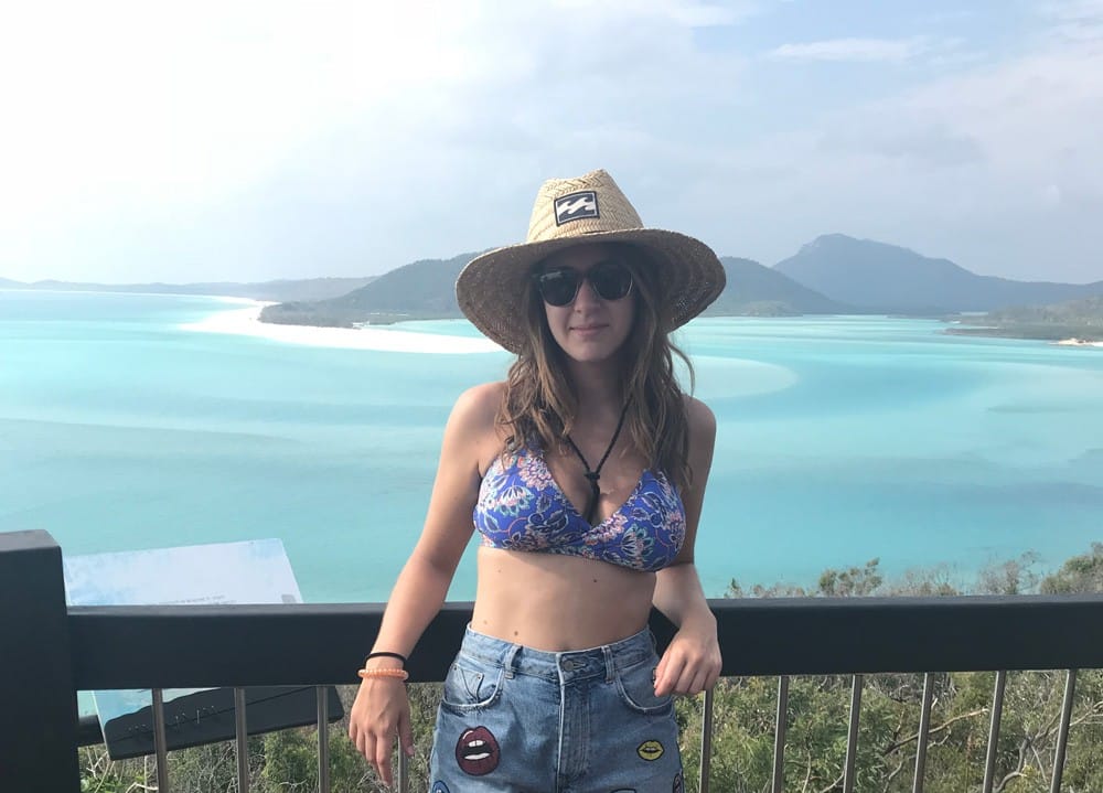 chica rubia en bikini con sombrero de paja en un mirador con el mar paradisíaco de las Whitsundays detrás